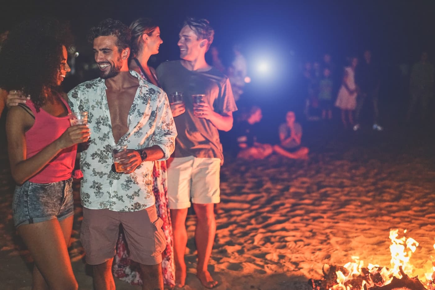 Friends with drinks around a fire on a beach at night